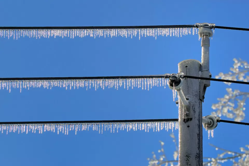 Power lines with dense icicles hanging from them against blue sky.